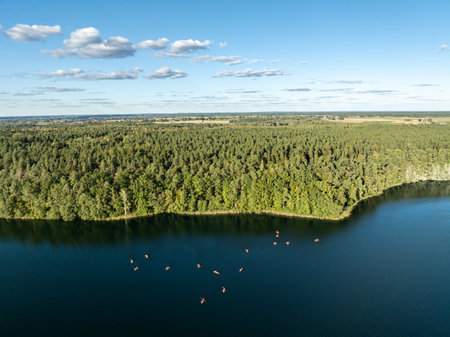 Aerial drone view of people kayaking on a lake surrounded by green forest. Sailing in red kayaks in the Masurian Lake District. Lake Lesk in the Kulka Reserve in Poland.の写真素材