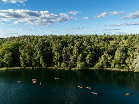 Aerial drone view of people kayaking on a lake surrounded by green forest.Sailing in red kayaks in the Masurian Lake District. Lake Lesk in the Kulka Reserve in Poland.Kulka Reserve, Masuria, Poland.の写真素材