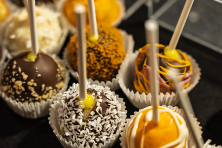 Decorative chocolate pops on sticks with vibrant colors and toppings arranged on a clear display stand. Colorful chocolate lollipops with chocolate sprinkles and other sweet toppingsの写真素材