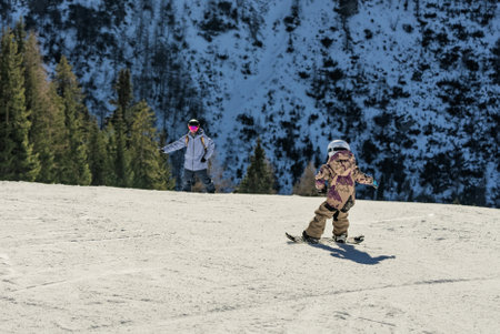 Group of people snowboarding in mountains on a sunny winter day. Snowboard lessons with local instructors. Children learn to snowboard with an instructor. Children snowboarding in the Dolomites Alps.の写真素材