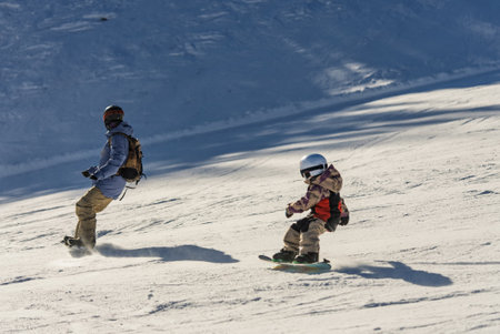 Group of people snowboarding in mountains on a sunny winter day. Snowboard lessons with local instructors. Children learn to snowboard with an instructor. Children snowboarding in the Dolomites Alps.の写真素材
