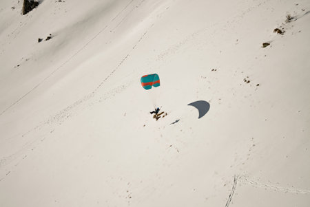 Paraglider soaring through the clouds above a snowy mountain range. Paraglider above clouds with a dramatic sky backdrop. Paragliders preparing for takeoff on a snowy slope in the mountains.の写真素材