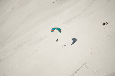 Paraglider soaring through the clouds above a snowy mountain range. Paraglider above clouds with a dramatic sky backdrop. Paragliders preparing for takeoff on a snowy slope in the mountains.の写真素材