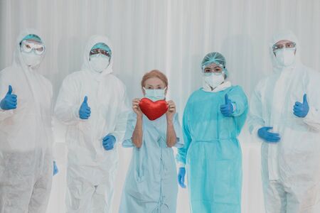 Old woman patient hold mini heart with background of the medical team thumbs up after recovered from...