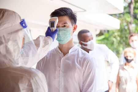 Line up for Social distancing concept. Officer use infrared forehead thermometer to check fever body...