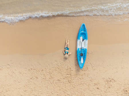 Beautiful woman in bikini lying on the beach with a kayak besideの写真素材