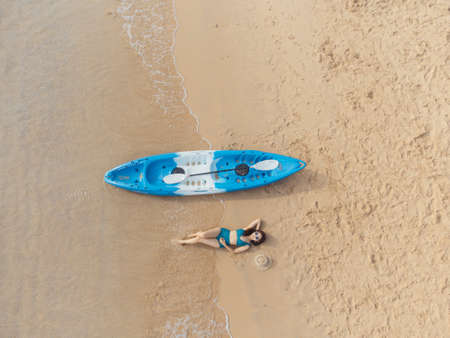 Beautiful woman in bikini lying on the beach with a kayak besideの写真素材