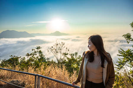 Asian woman with background of Sea of Fog covers and golden sunrise the area on the top of hill Doi Phu Thok, Chiang Khan, Loei, Thailand.の写真素材
