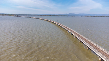 Aerial view of an amazing travel train parked on a floating railway bridge over the water of the lake in Pa Sak Jolasid dam with blue sky at Lopburi, Thailand.の写真素材
