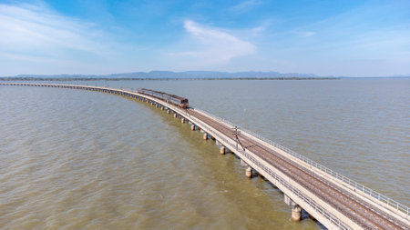 Aerial view of an amazing travel train parked on a floating railway bridge over the water of the lake in Pa Sak Jolasid dam with blue sky at Lopburi, Thailand.の写真素材