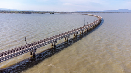 Aerial view of an amazing travel train parked on a floating railway bridge over the water of the lake in Pa Sak Jolasid dam with blue sky at Lopburi, Thailand.の写真素材