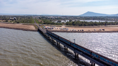 Aerial view of an amazing travel train parked on a floating railway bridge over the water of the lake in Pa Sak Jolasid dam with blue sky at Lopburi, Thailand.の写真素材