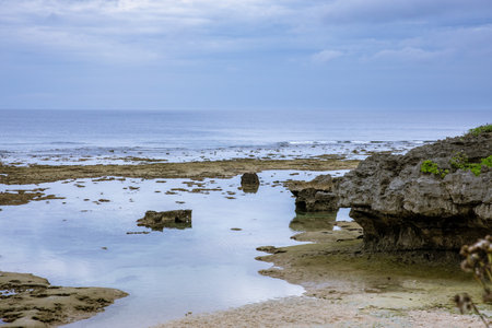 Atmosphere of the sea in Okinawa beach features crystal-clear water, visible rocks, and waves gently hitting the shoreline.の写真素材