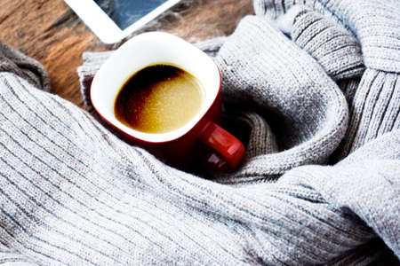 Top view of cup of coffee on gray knitted sweater - Wooden table - Red glass