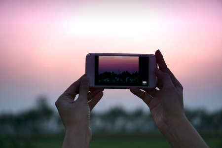 Girl takes pictures of a nature sunset on the smart phone - Woman hand raising her smartphone up...