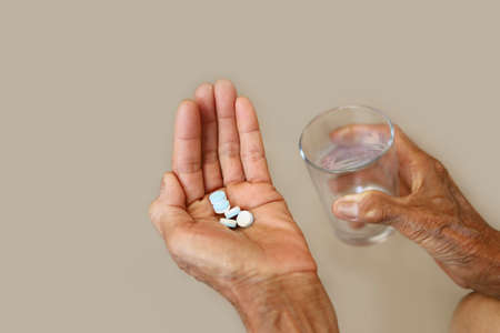 Many pills in a seniorâ€™s hands with glass of water. Painful old age. Caring for the health of...