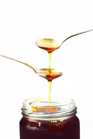 Honey drop in a spoon, glass bottle isolated on white backgroundの写真素材