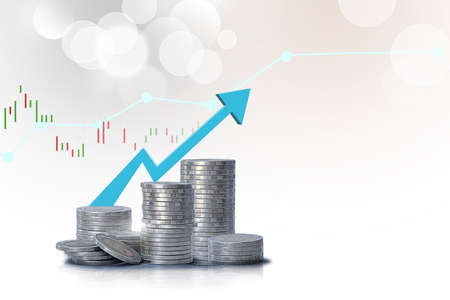 Stacks of gold coins on table and raising arrow over economic charts on white background - Saving money conceptの写真素材