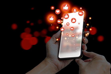 Hand holding smartphone with social media icon on screen and black background.