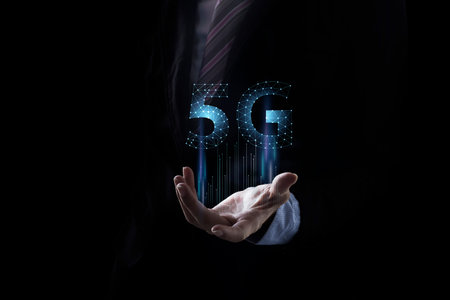 Businessman hand holding 5G icon in screen on dark background.