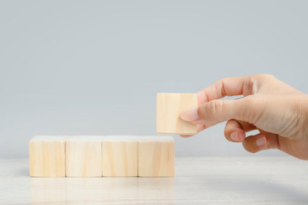Hand arranging wood block stacking as step stair on gray background, business growth concept. Blank wood cube block backgroundの写真素材
