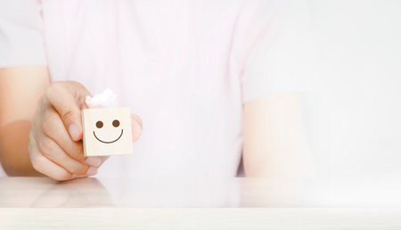 Woman hand holding a wooden cube with a smiley face icon over white background. customer services...