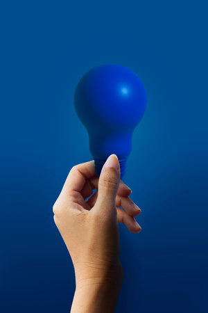 Hand holding blue lightbulb on blue background, Energy saving conceptの写真素材