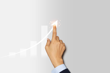 Hand draws a rising arrow on blue background. Finger pointing on the shining arrowhead, minimal style.の写真素材