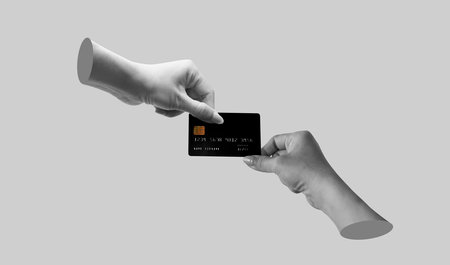 Black plastic credit card is in the hands of two women holding different sides isolated on a grey backgroundの写真素材