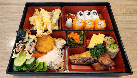 A vibrant Japanese bento box featuring an assortment of sushi, tempura, fresh vegetables, and grilled fish, perfect for lunch or dinner.の写真素材