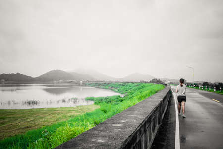 Young women walking on streets of large reservoirs with the mountain early in the morning at Thailand, color effect photo.の写真素材