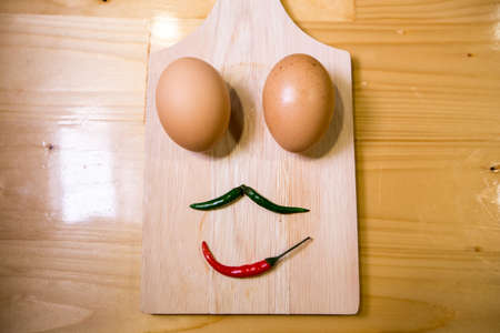 Low key- Eggs and chili scowl emotion on the wood.の写真素材