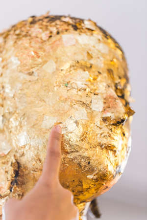 Women hand putting gold leaf onto The Buddha statue to gild. Which people use to worship the buddha image. Selective focus.の写真素材