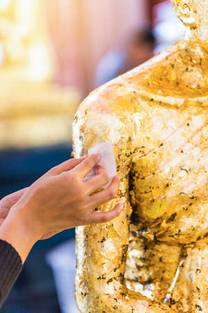 Women hand puting gold leaf onto The Buddha statue to gild. Which people use to worship the buddha...