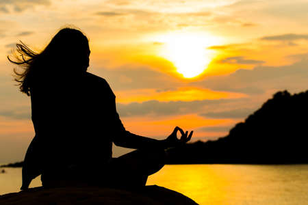 Silhouette, Woman Meditating in Yoga pose or Lotus Position by the Sea at Sunset. Rear View. Nature Meditation Concept. Low key photo. relax time.の写真素材