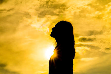 Silhouette of young woman standing at relax pose or freedom pose or chill pose on the beach during sunset.の写真素材