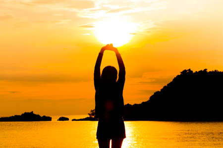 Silhouette of young woman standing at relax pose or freedom pose or chill pose on the beach during...