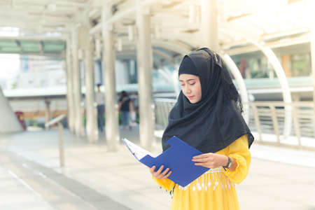 Young asian muslim business woman smiling and holding file document and standing at capital city. Beautiful muslim women. Thai muslim women.の写真素材