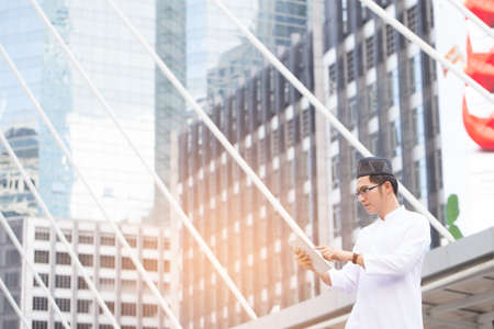 Young handsome businessman Arab Muslims looking at his business report in his tablet by internet network while standing at central of city. Business and technology concept.の写真素材