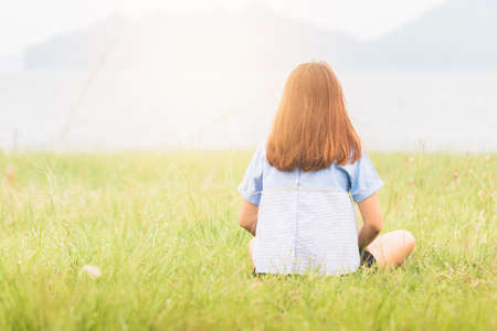Young woman sitting at relax pose or freedom pose or chill pose on the meadow during sunrise at morning. Riverside.の写真素材