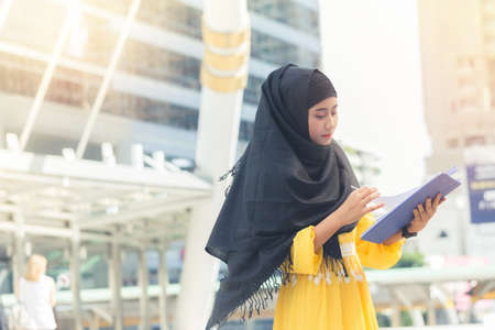Young asian muslim business woman smiling and holding file document and standing at capital city. Beautiful muslim women. Thai muslim women.の写真素材