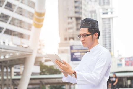 Young handsome businessman Arab Muslims looking at his business report in his tablet by internet network while standing at central of city. Business and technology concept.の写真素材