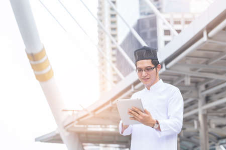 Young handsome businessman Arab Muslims looking at his business report in his tablet by internet network while standing at central of city. Business and technology concept.の写真素材
