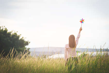 Silhouette of Beautiful girl holding wind toy or wind turbine or pinwheel and wool hat at meadow on winter season in morning.の写真素材
