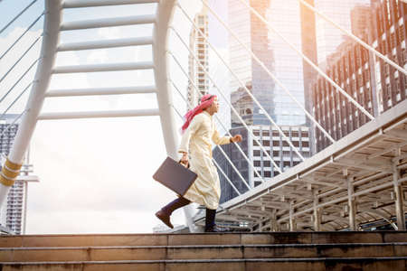 Young Muslim business man  holding bag and running rapidly to airport. In rush hour at stairway in urban. Business in the city concept.の写真素材