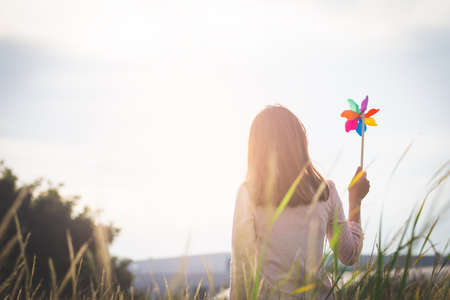 Silhouette of Beautiful girl holding wind toy or wind turbine or pinwheel and wool hat at meadow on winter season in morning.の写真素材