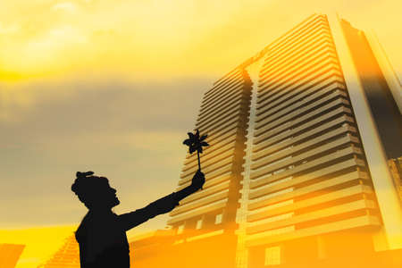 Silhouette of Beautiful girl holding wind toy or wind turbine or pinwheel and wool hat at city on winter season in morning.の写真素材