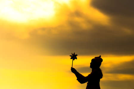 Silhouette of Beautiful girl holding wind toy or wind turbine or pinwheel and wool hat at meadow on winter season in morning.の写真素材
