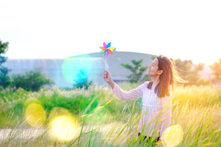 Silhouette of Beautiful girl holding wind toy or wind turbine or pinwheel and wool hat at meadow on winter season in morning.の写真素材