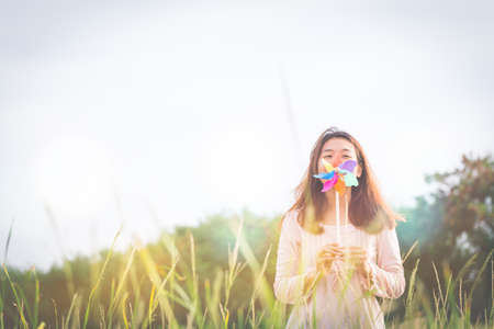 Silhouette of Beautiful girl holding wind toy or wind turbine or pinwheel and wool hat at meadow on winter season in morning.の写真素材